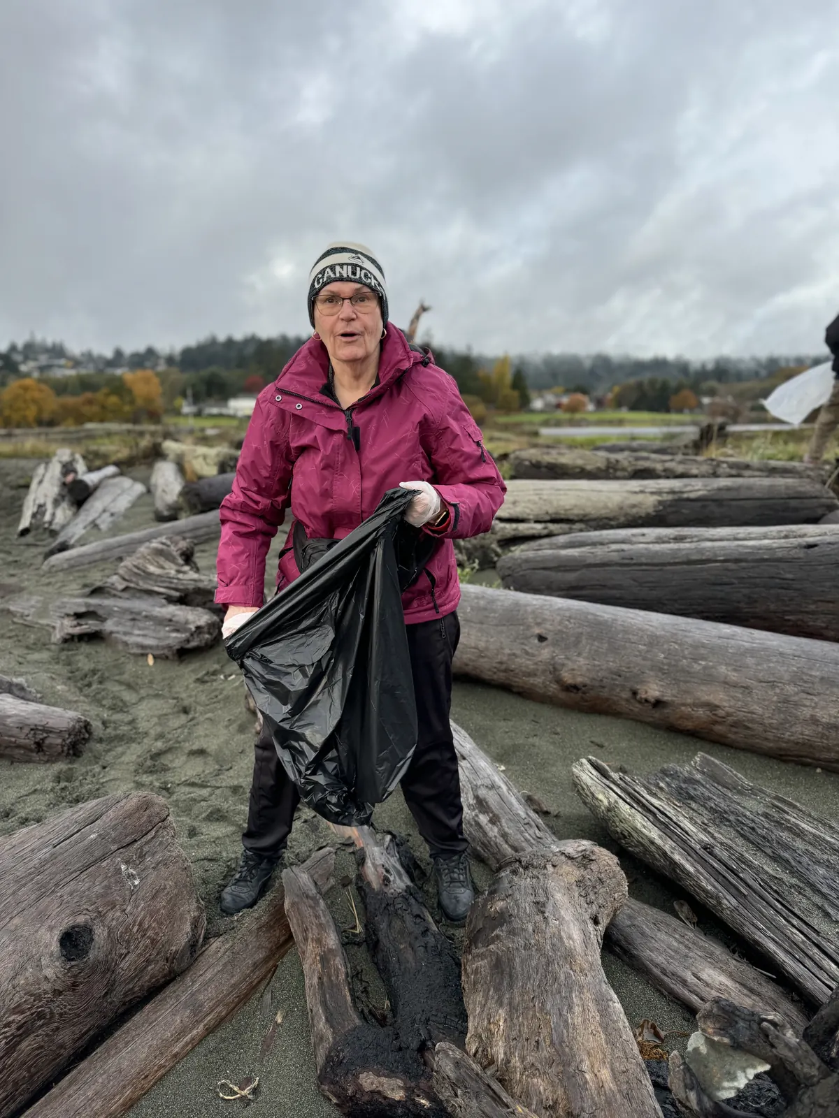 A member holding a garbage bag on a driftwood beach