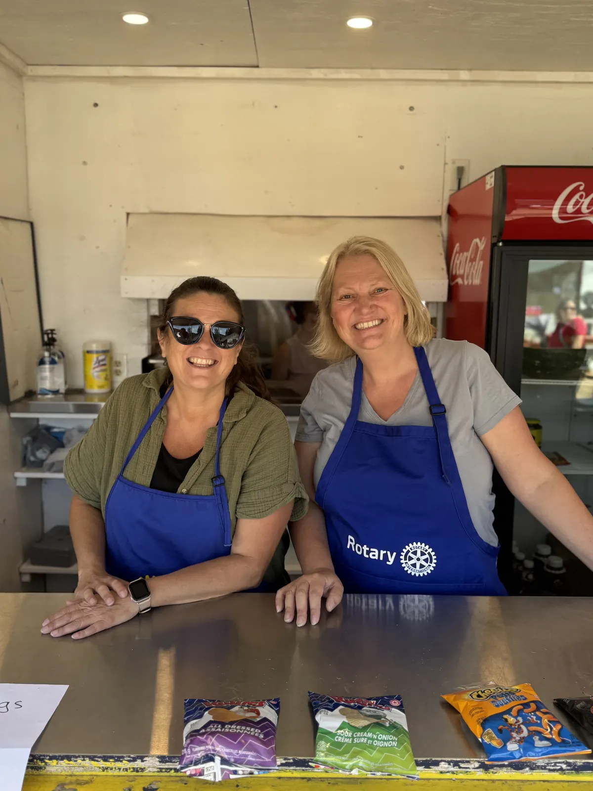 Two smiling Rotarians in blue aprons at a concession stand