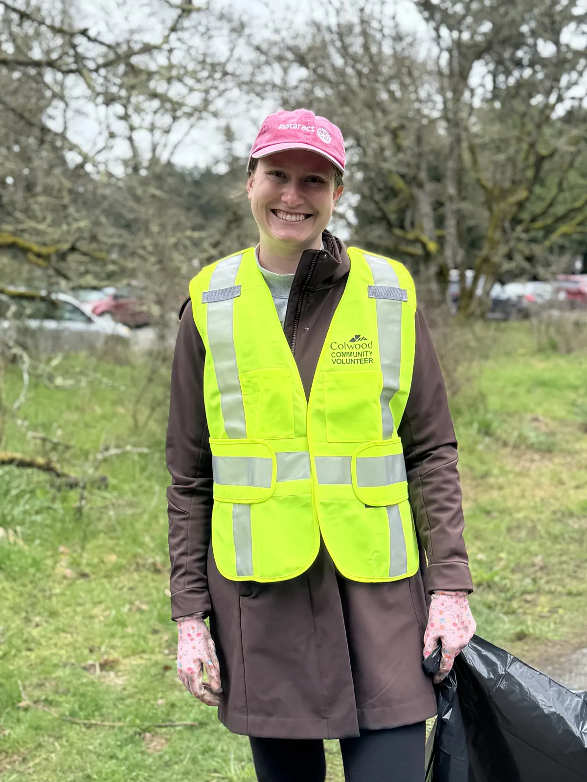 A smiling member in a Rotaract cap and safety vest at a cleanup